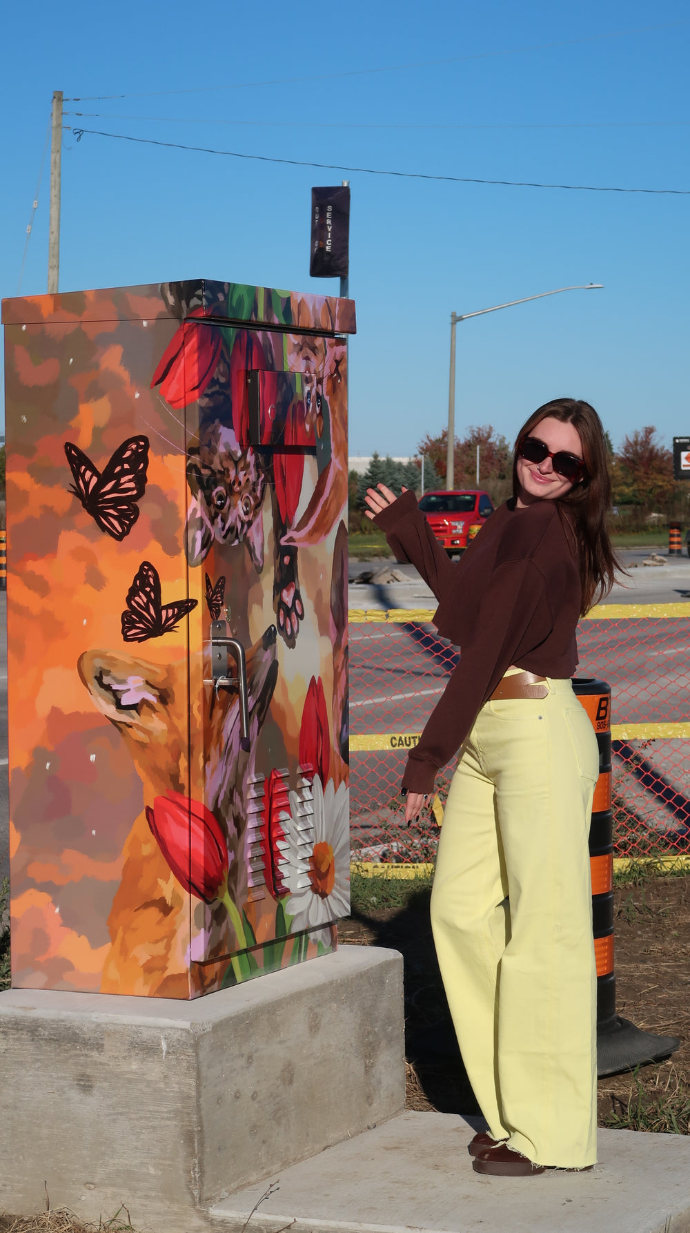 Sam standing next to a her colourful animal mural on the city of Barries traffic cabinet on Mapleview Drive