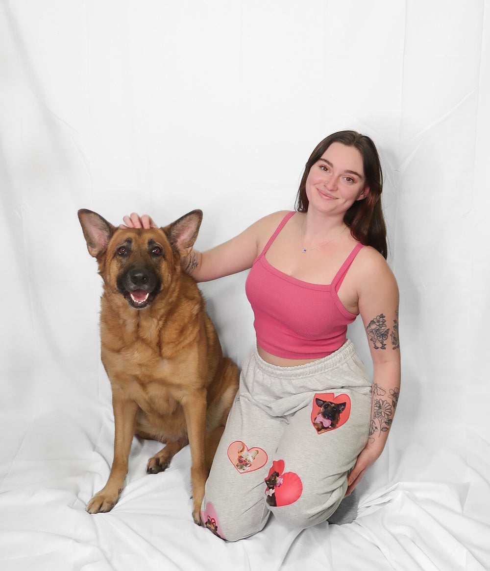 Sam in pink top and puppy love  track pants sitting next to her German Shepherd dog Skylar on a white background